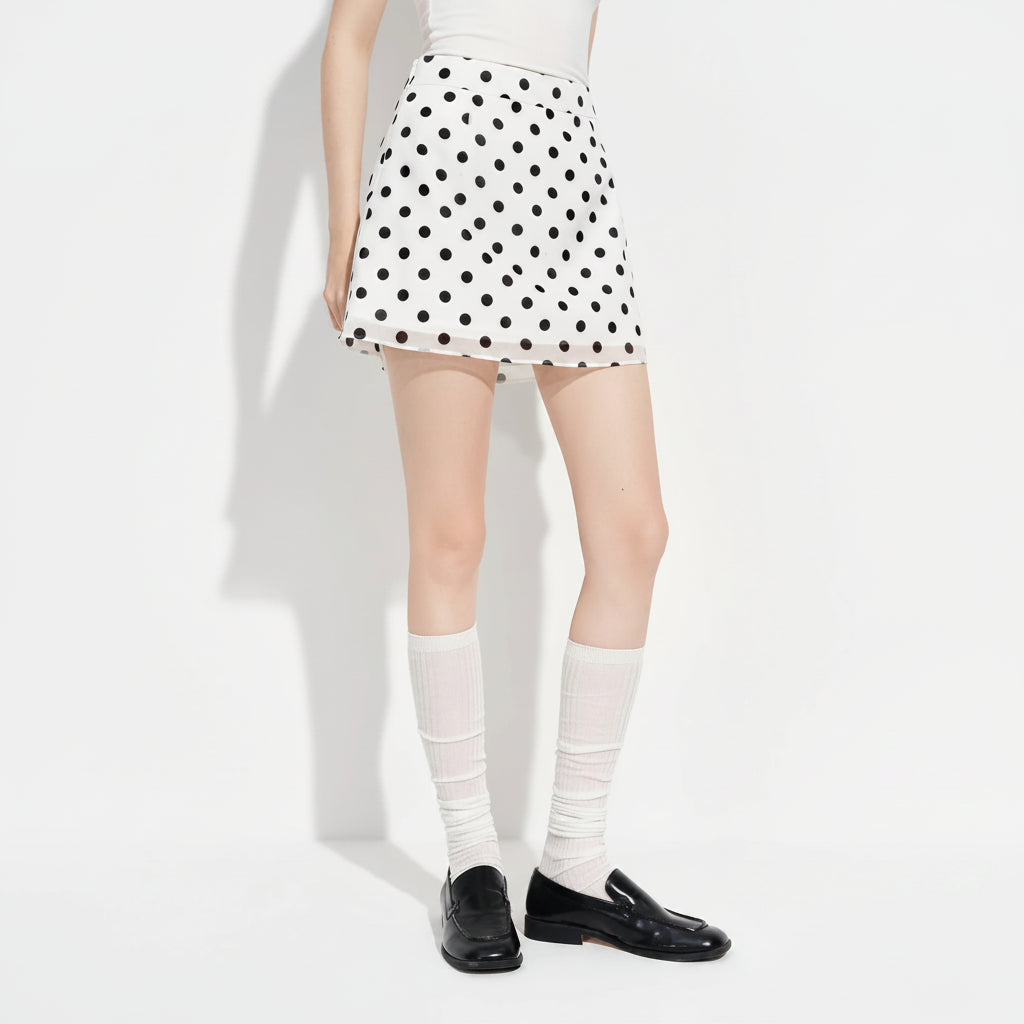 A model wearing a white A-line mini skirt with black polka dots, paired with white knee-high socks and black leather loafers. The brand logo 'fsle' is visible in the top left corner.