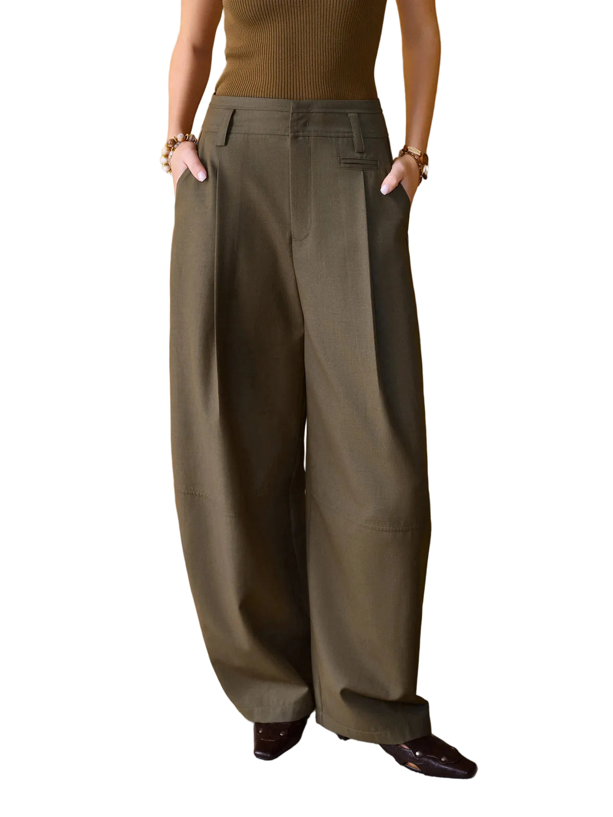A model wearing a pair of wide-leg, high-waisted olive green trousers, paired with a brown ribbed top and dark brown pointed-toe loafers, standing against a textured mustard yellow wall.