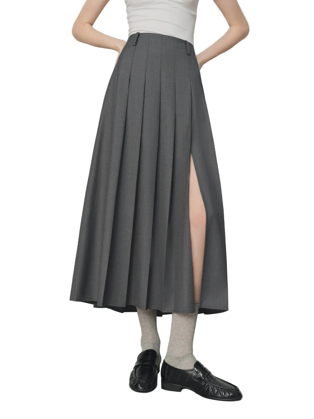 Person wearing a gray pleated skirt with a white top and black shoes on a plain background