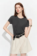 A woman modeling a dark charcoal gray short-sleeve crewneck t-shirt, paired with cream-colored high-waisted shorts and a black belt, against a plain white studio background. The brand logo 'fsle' is visible in the top left corner.