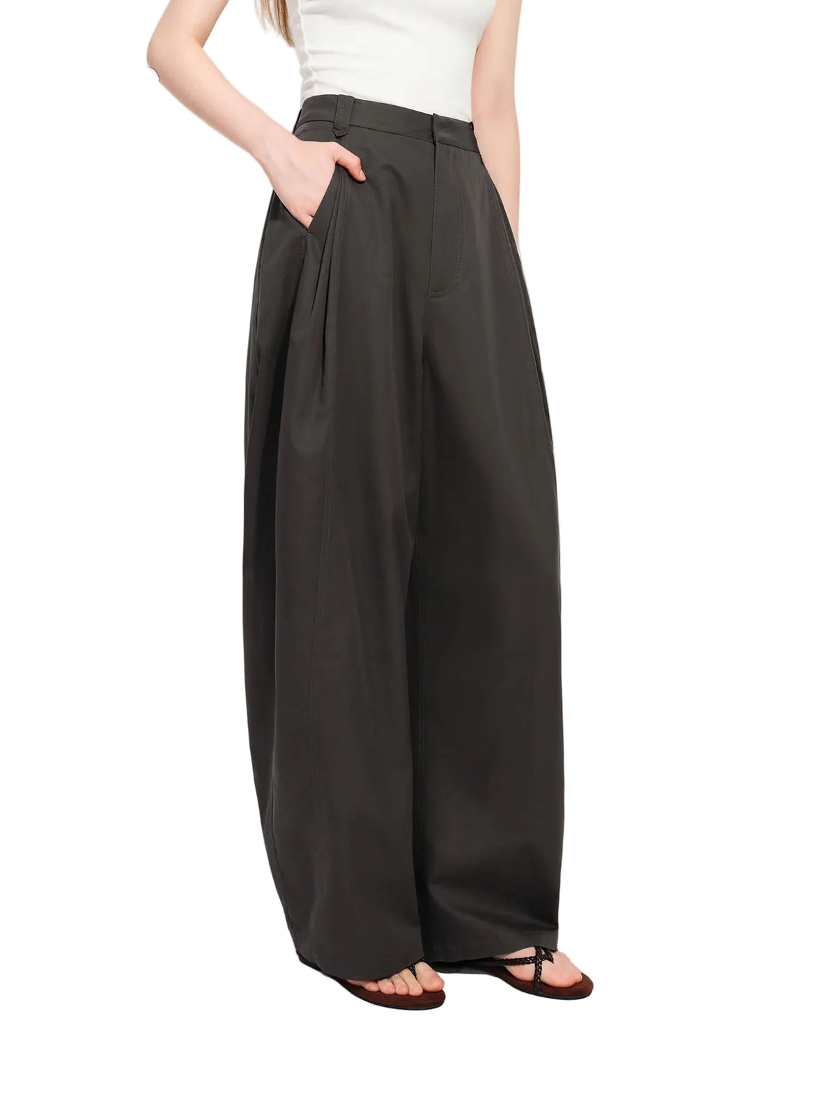 A model wearing high-waisted, wide-leg charcoal gray pants with a white top and brown sandals, shown from the waist down against a white studio background with a soft shadow.